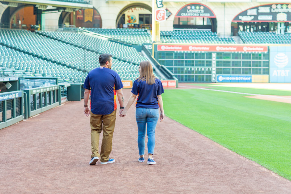 Engaged couple walking hand in hand in an empty field at Minute Maid Park